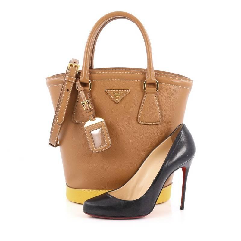 This authentic Prada Lux Convertible Bucket Tote Bicolor Saffiano Leather Medium is refined and bold in design made for the modern woman. Crafted from light brown saffiano leather with yellow leather base, this structured bucket shaped tote features