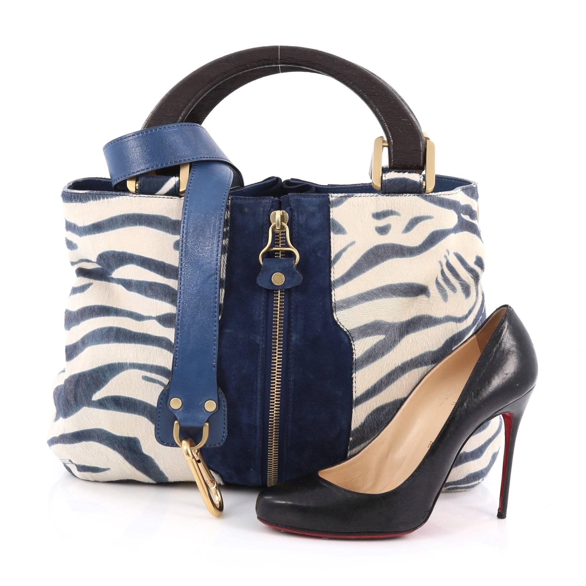 This authentic Jimmy Choo Maia Tote Pony Hair Medium is an eye catching piece perfect for bold fashionistas. Crafted in blue and white genuine pony hair, this bag features dual wooden handles, detachable strap, front and back extension zippers and