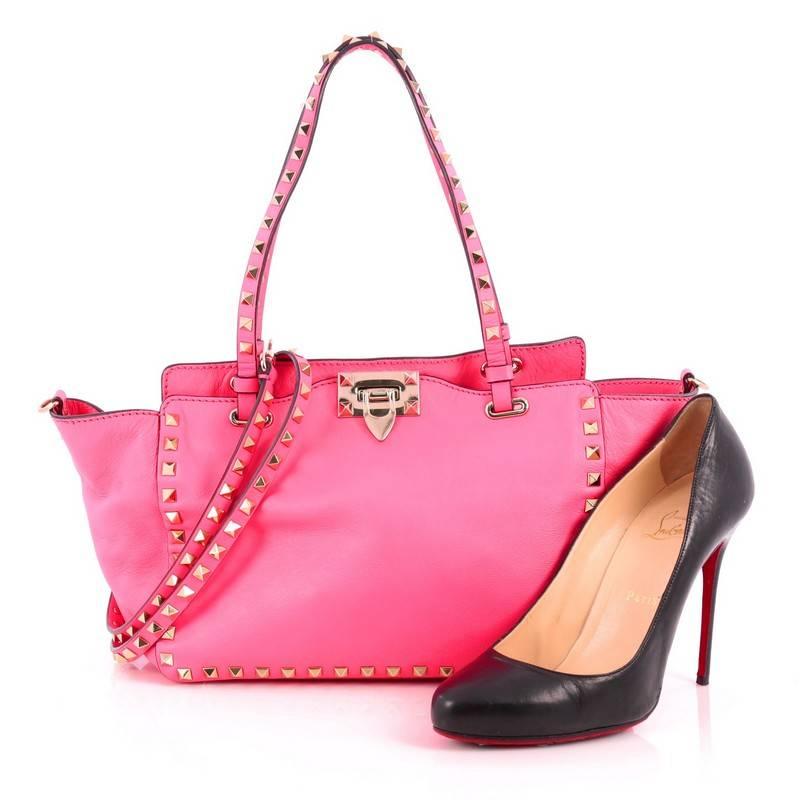 This authentic Valentino Rockstud Tote Soft Leather Small mixes edgy style with luxurious detailing. Crafted from neon pink soft leather, this stylish tote features dual tall flat handles, gold-tone pyramid stud trim details, signature clasp