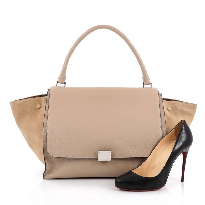 This authentic Celine Trapeze Handbag Leather Large is a modern minimalist design with a playful twist in subdued colors. Crafted from taupe leather and beige suede wings, this classic tote features a top rolled handle, side snap closures, exterior