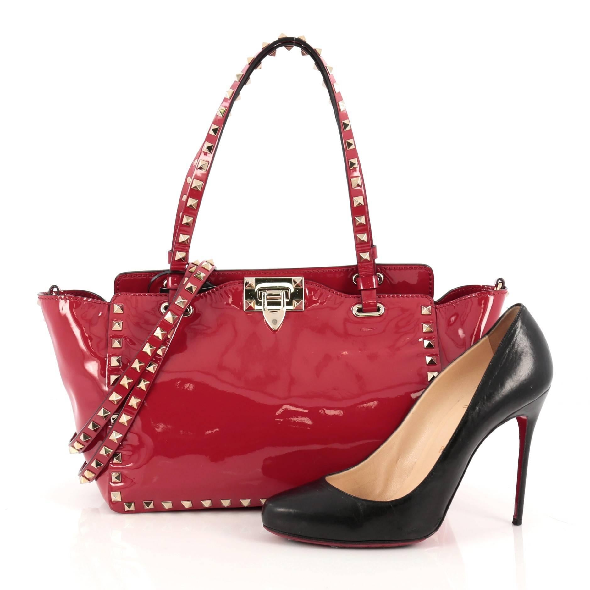 This authentic Valentino Rockstud Tote Soft Patent Small mixes edgy style with luxurious detailing. Crafted from red soft patent leather, this stylish tote features dual tall flat handles, gold-tone pyramid stud trim details, signature clasp