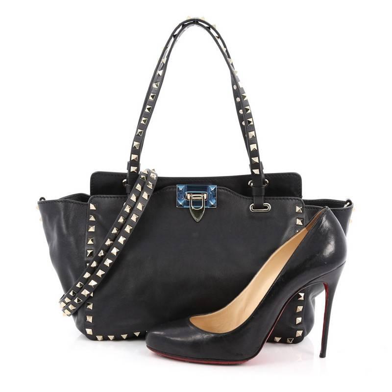 This authentic Valentino Rockstud Tote Soft Leather Small mixes edgy style with luxurious detailing. Crafted from black soft leather, this stylish tote features dual tall flat handles, gold-tone pyramid stud trim details, signature clasp fastening,