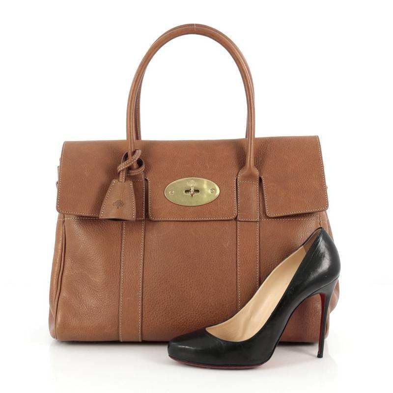 This authentic Mulberry Bayswater Satchel Leather Medium showcases the brand's simple, iconic design made for everyday use. Crafted from brown leather, this industrial-style tote features tall dual-rolled leather handles, protective base studs, and