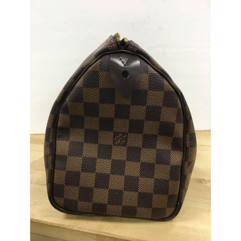 This authentic Louis Vuitton Speedy Handbag Damier 25 is a timeless favorite of many. Constructed from Louis Vuitton's signature damier ebene coated canvas, this iconic Speedy features dual-rolled handles, brown leather trims and gold-tone hardware