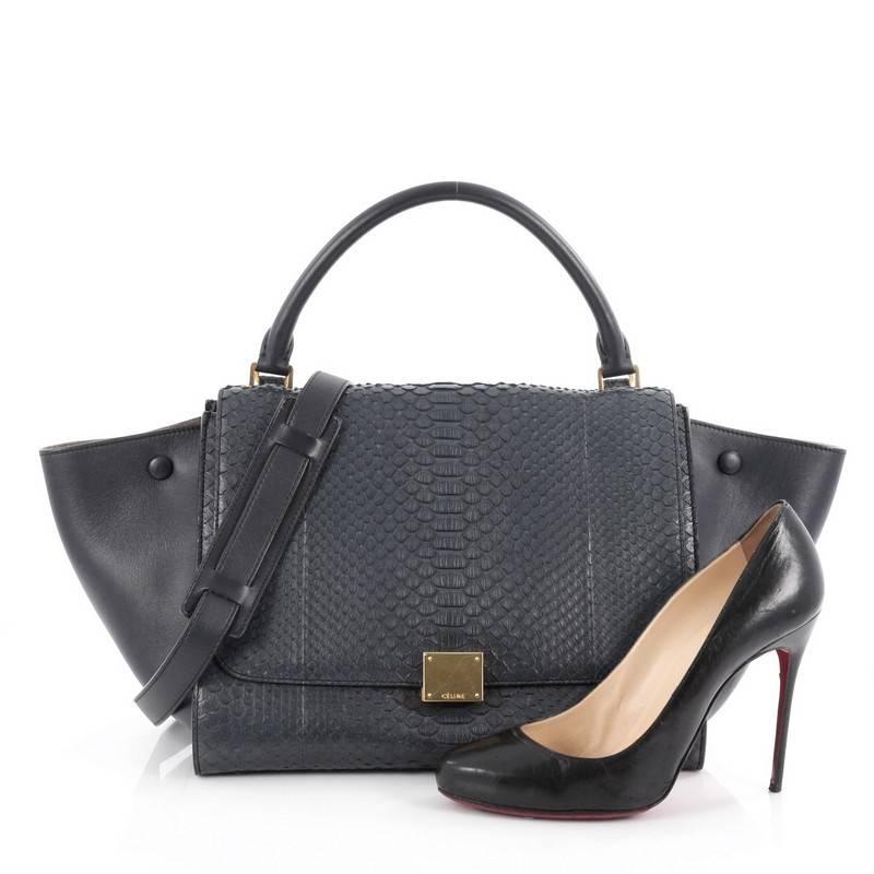 This authentic Celine Trapeze Handbag Python Medium is a fashionista's dream. Crafted in genuine navy blue python skin with leather wings, this stylish bag features exterior back zip pocket, top handle with removable shoulder strap and gold-tone