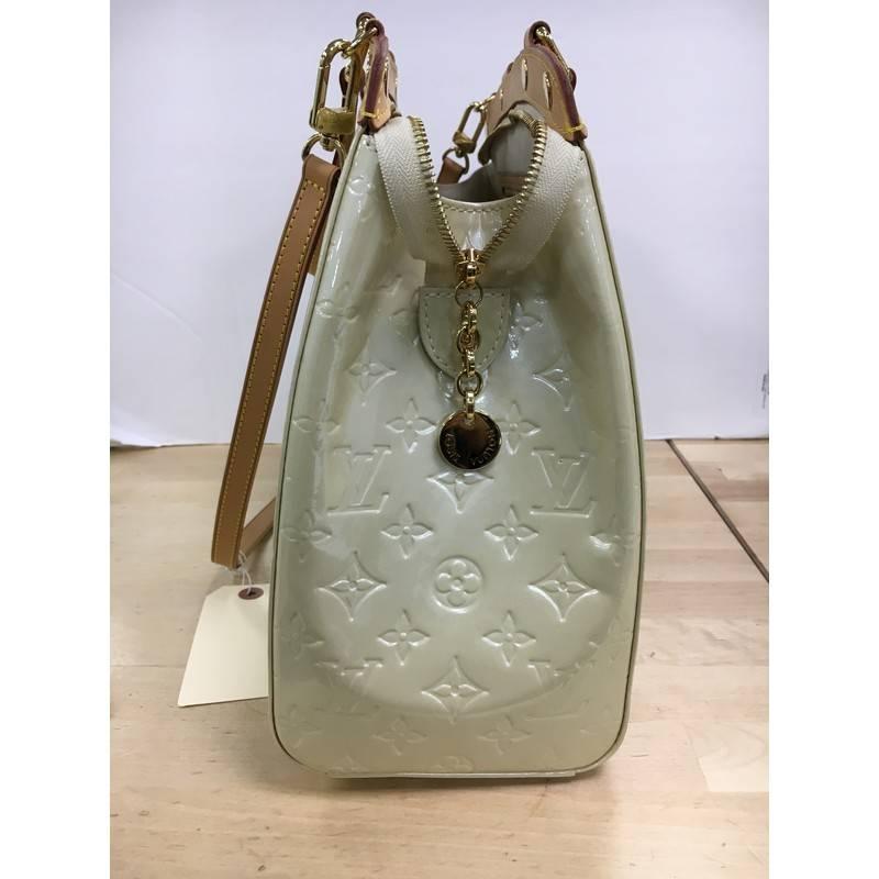 This authentic Louis Vuitton Brea Handbag Monogram Vernis GM is a staple for an everyday casual look. Crafted in pearlescent cream monogram vernis with cowhide leather trims, this structured yet feminine tote features dual flat handles, stand-out