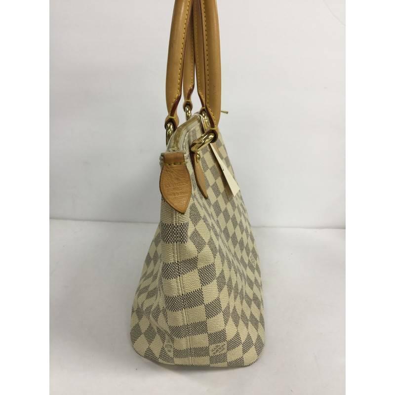 This authentic Louis Vuitton Saleya Handbag Damier PM is a mix of classic style with modern functionality. Crafted from damier azur coated canvas, this tote features dual-rolled vachetta leather tall handles, structured base, and gold-tone hardware
