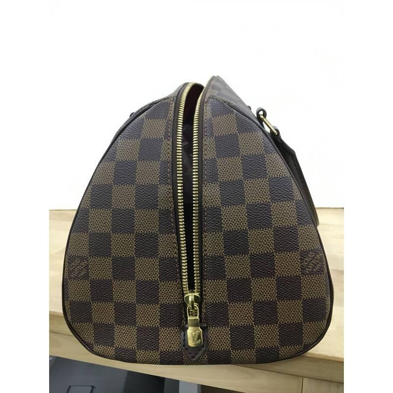 This authentic Louis Vuitton Ribera Handbag Damier MM is a chic easy to carry top handle. Crafted from Louis Vuitton's signature damier ebene coated canvas, this neatly structured and modern dome satchel features dual-rolled dark brown leather
