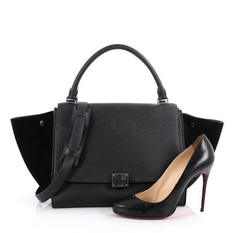 This authentic Celine Trapeze Handbag Leather Medium is a fashionista's dream. Crafted in black leather with suede wings, this classic bag features exterior back pocket, top handle with removable shoulder strap and silver-tone hardware accents. Its
