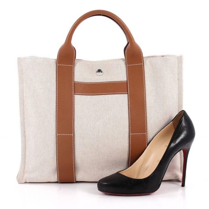 This authentic Hermes Sac Harnais Tote Toile and Leather MM is an elegant and simple tote made for all seasons. Crafted from natural toile canvas with gold clemence leather trims, this chic everyday tote features dual-flat leather handles, a top