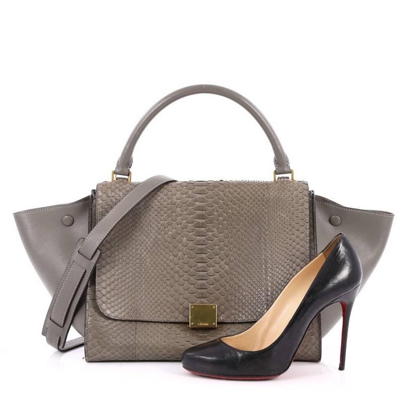 This authentic Celine Trapeze Handbag Python Small is a fashionista's dream. Crafted in genuine grey python skin with leather wings, this stylish bag features exterior back zip pocket, top handle with removable shoulder strap and gold-tone hardware