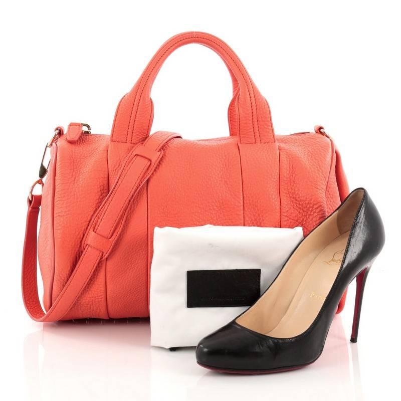 This authentic Alexander Wang Rocco Satchel Leather is fashion-forward, tasteful and makes a bold statement. Crafted from coral leather, this edgy duffle bag features dual flat leather handles, signature base studs detail and gold-tone hardware