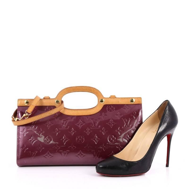 This authentic Louis Vuitton Roxbury Drive Handbag Monogram Vernis showcases a unique boxy, triangular silhouette. Constructed from purple monogram vernis, this bag features flat vachetta leather handles and trims, stud detailing, and gold-tone