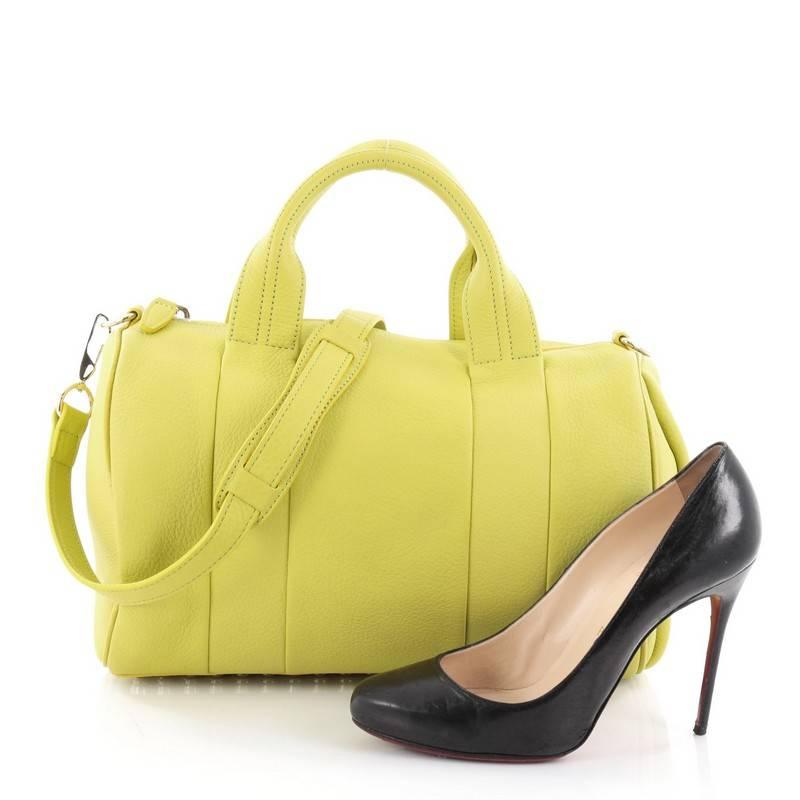 This authentic Alexander Wang Rocco Satchel Leather is fashion-forward, tasteful and makes a bold statement. Crafted from citron leather, this edgy duffle bag features dual flat leather handles, signature base studs detail and gold-tone hardware