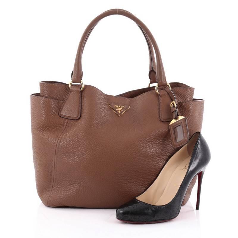 This authentic Prada Side Pocket Convertible Tote Vitello Daino Large is a simple, stylish tote made for everyday use. Crafted from medium brown vitello daino leather, this bag features dual-rolled leather handles, raised Prada logo at the center,