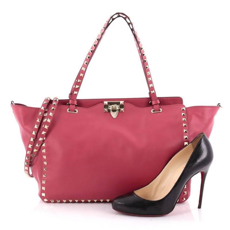 This authentic Valentino Rockstud Tote Soft Leather Medium mixes edgy style with luxurious detailing. Crafted from pink soft leather, this stylish tote features dual tall flat handles, gold-tone pyramid stud trim details, a signature clasp