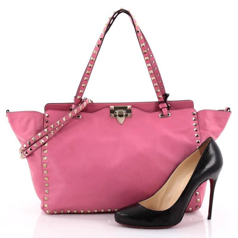 This authentic Valentino Rockstud Tote Soft Leather Medium mixes edgy style with luxurious detailing. Crafted from neon pink soft leather, this stylish tote features dual tall flat handles, gold-tone pyramid stud trim details, a signature clasp