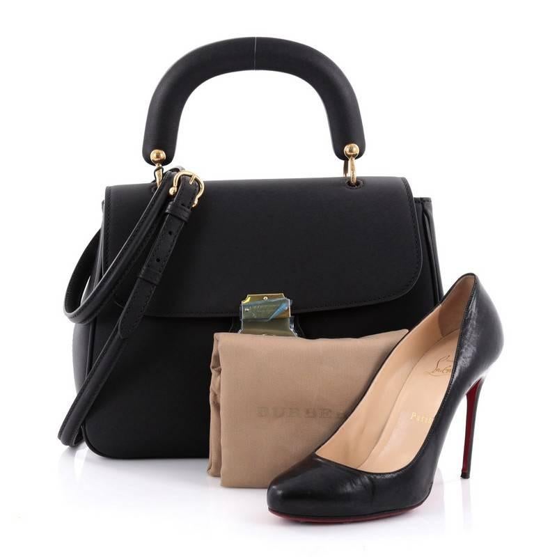 This authentic Burberry DK88 Top Handle Bag Leather Medium displays a timeless silhouette that reflects the British sensibility. Crafted from black leather, this chic bag features a structured top handle, detachable strap, front flap with