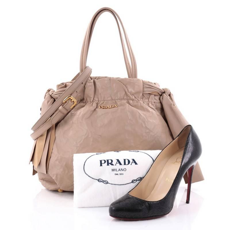 This authentic Prada Convertible Bow Tie Shoulder Bag Leather Medium is elegant in its simplicity and structure. Crafted from beige soft leather, this feminine tote features dual tall flat handles, gold Prada logo, subtle Prada Milano embroidered