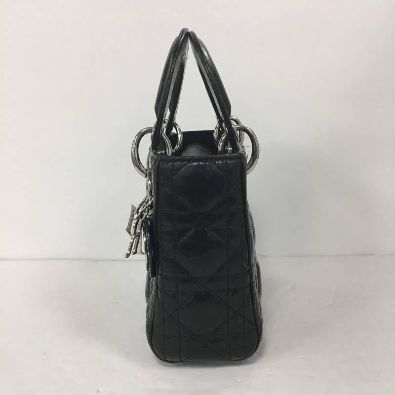 This authentic Christian Dior Lady Dior Handbag Cannage Quilt Lambskin Mini is an elegant classic bag that every fashionista needs in her wardrobe. Crafted from black lambskin leather in Dior's iconic cannage quilting, this boxy bag features short