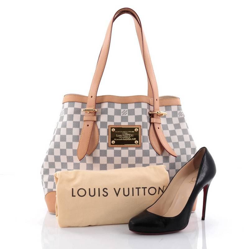 This authentic Louis Vuitton Hampstead Handbag Damier MM is a luxurious, city tote that showcases modern structure. Crafted from the brand’s damier azur canvas, this tote features dual tall flat vachetta leather handles with buckle details, vachetta
