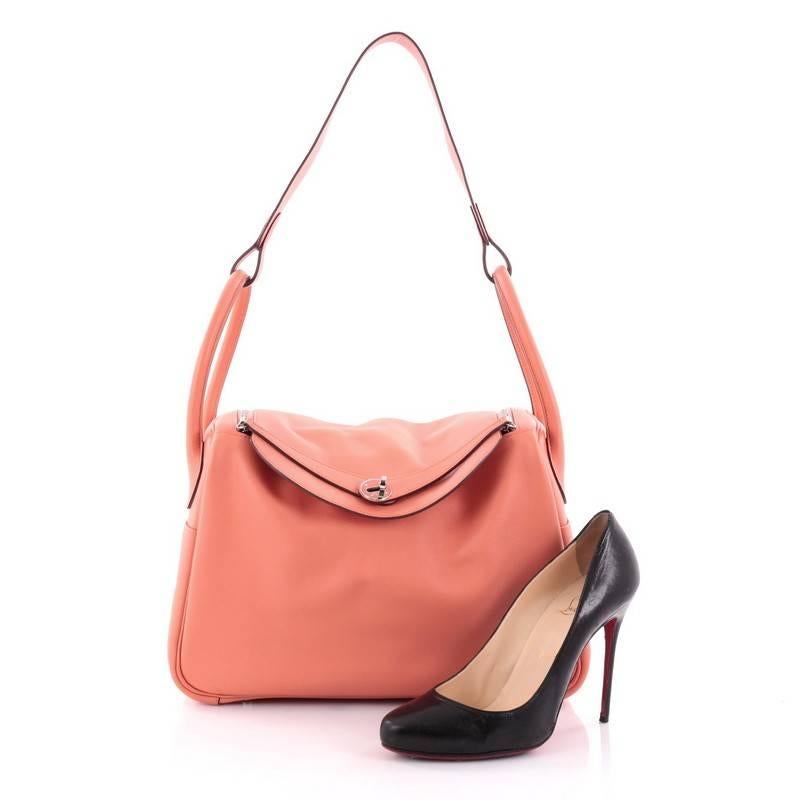 This authentic Hermes Lindy Handbag Evercolor 34 is the perfect understated accessory for the modern woman. Crafted from flamingo evercolor leather, this no-fuss shoulder bag features dual rolled handles, two sides slip pockets, protective base