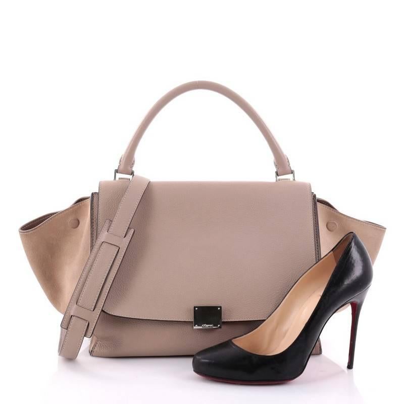 This authentic Celine Trapeze Handbag Leather Medium is a fashionista's dream. Crafted in light taupe leather with beige suede wings, this classic bag features silver-tone hardware accents, exterior back pocket, leather top handle, and removable