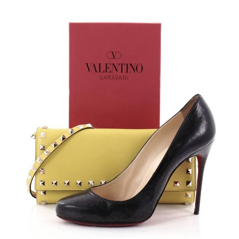 This authentic Valentino Rockstud Trifold Wallet on Strap Leather is a sleek and beautiful clutch that will keep you organized. Crafted from yellow leather, this chic clutch features removable studded strap, signature rockstud trims, front flap with