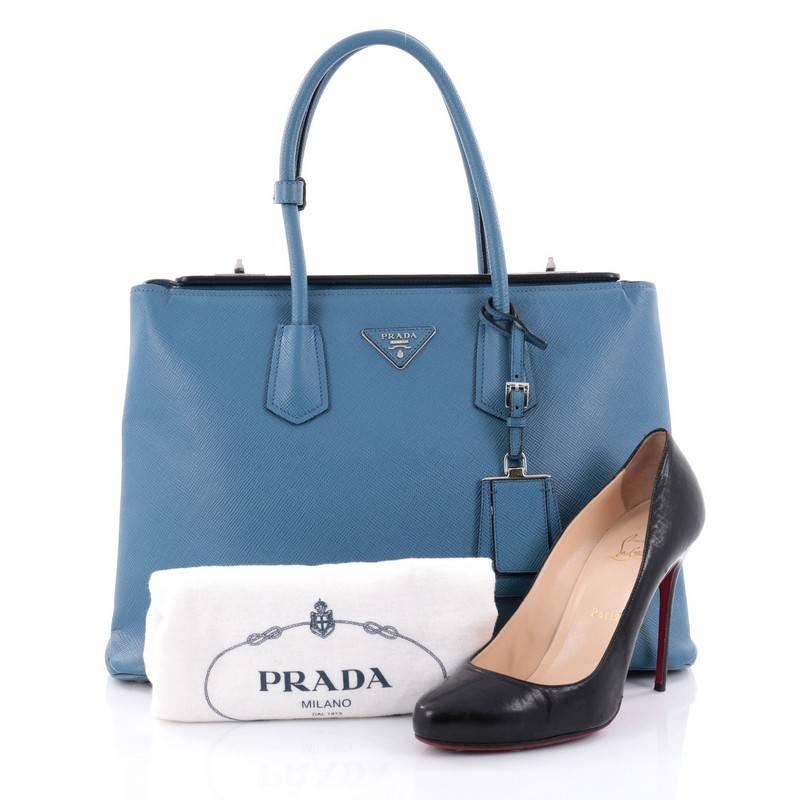 This authentic Prada Turnlock Twin Tote Saffiano Leather Medium stylish bag is perfect to carry around from day to night. Crafted from blue saffiano leather, this tote features dual-rolled leather handles, angular silhouette, inverted triangle Prada
