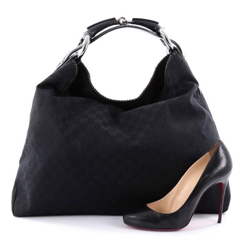 This authentic Gucci Horsebit Hobo GG Canvas Large is an easy to carry, everyday hobo that is both stylish and functional. Crafted in Gucci's black monogram GG canvas, this no-fuss hobo features a signature horsebit top handle strap, edge leather