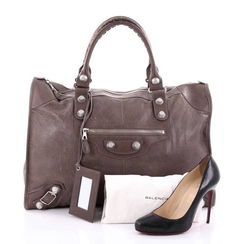This authentic Balenciaga Weekender Giant Studs Handbag Leather is a stylish and fun duffle made for light travels and weekend getaways. Constructed from taupe leather, this lightweight bag features braided woven handle straps, front zipped pocket,