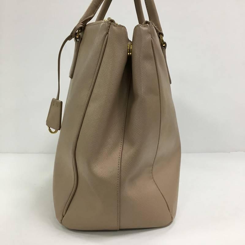 This authentic Prada Double Zip Lux Tote Saffiano Leather Large is the perfect bag to complete any outfit. Crafted from light pink saffiano leather, this boxy tote features side snap buttons, raised Prada logo, dual-rolled leather handles and