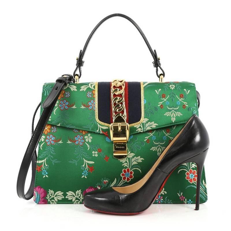 This authentic Gucci Sylvie Top Handle Bag Floral Jacquard Medium is perfect for modern fashionistas. Crafted from floral jacquard fabric with colorful flowers on a green fabric, this structured bag features a single looped leather handle, nylon web