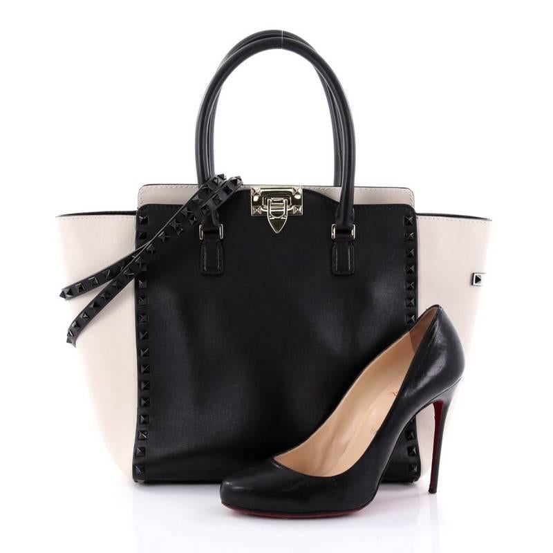 This authentic Valentino Rockstud Tote Rigid Leather Medium is a stylish and iconic bag that is one of today's most sought-after styles. Crafted from black and off-white rigid leather, this chic tote features signature black pyramid stud border,