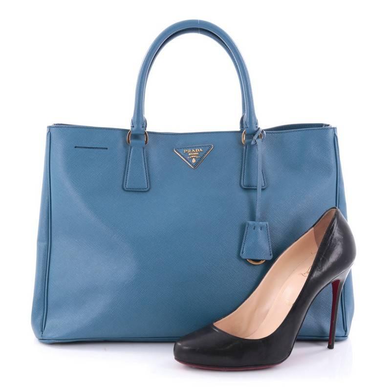 This authentic Prada Lux Open Tote Saffiano Leather Medium is elegant in its simplicity and structure. Crafted from blue saffiano leather, this sturdy and spacious tote features dual-rolled handles, gusseted side with snap buttons, iconic Prada logo