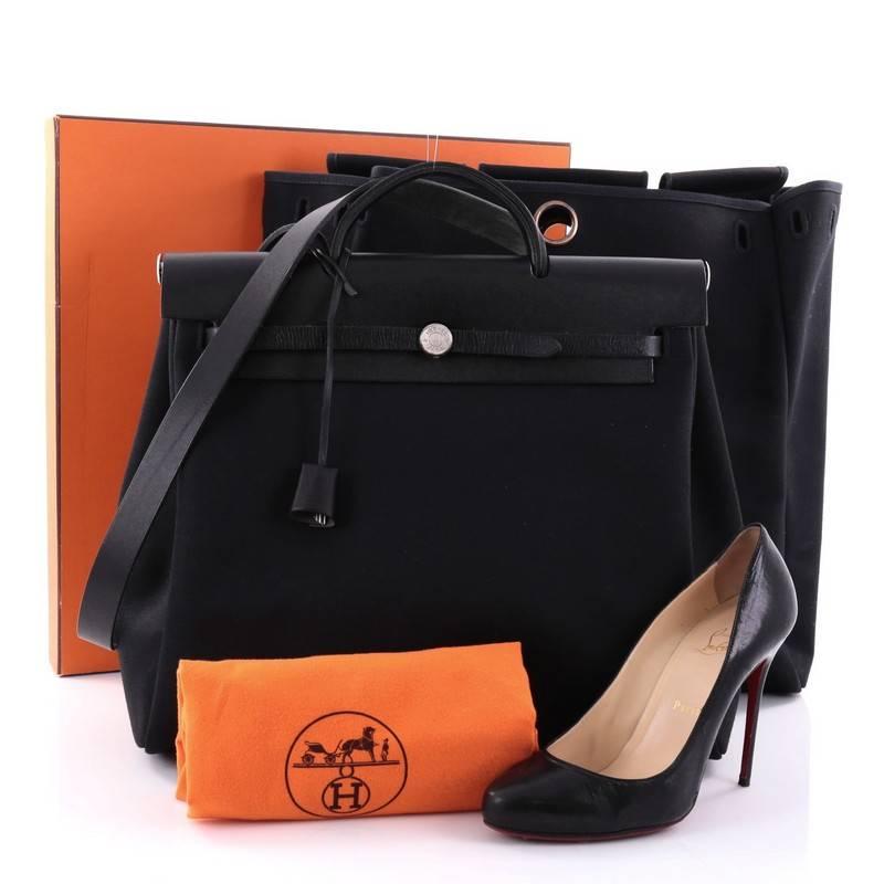 This authentic Hermes Herbag Toile and Leather MM is a fabulously functional Hermes set with two stylishly classic handbags fitting any mood. Constructed from sleek black vache hunter leather and toile canvas, this functional interchangeable bag