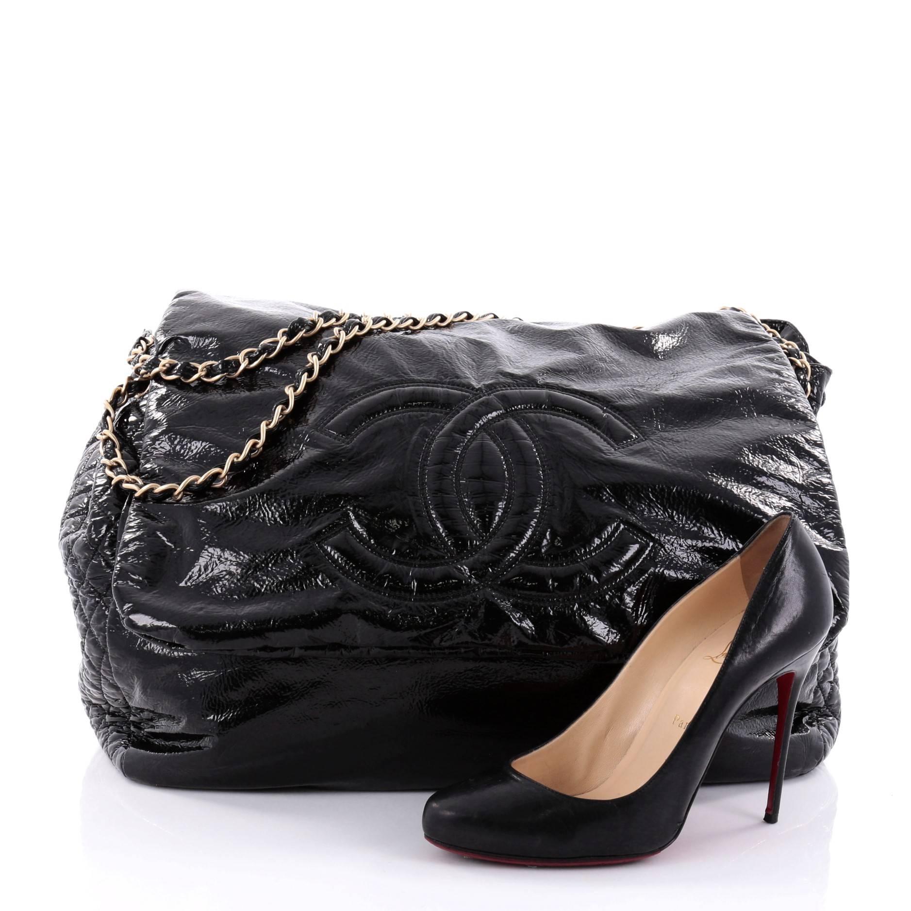 This authentic Chanel Rock and Chain Flap Bag Patent XL boasts an oversized stature perfect for Chanel lovers. Crafted in black patent leather, this maxi-sized tote features signature woven-in leather chain straps, large CC stitched design on its