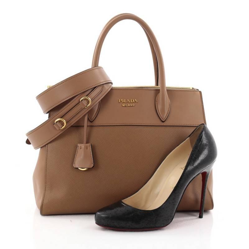 This authentic Prada Paradigme Handbag Saffiano Leather Medium is a timeless classic. Crafted from light brown saffiano leather with smooth calfskin leather trims, this bag features dual-rolled leather handles, signature Prada logo at top center,