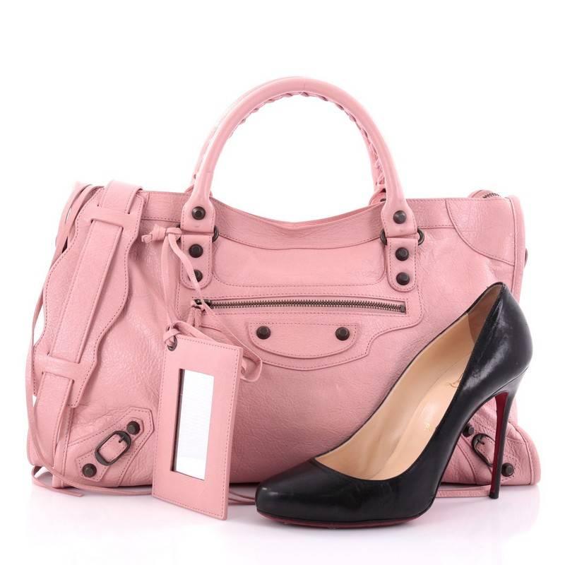This authentic Balenciaga City Classic Studs Handbag Leather Medium is for the on-the-go fashionista. Constructed in light pink leather, this popular bag features dual braided woven handle straps, front zip pocket, iconic Balenciaga classic studs