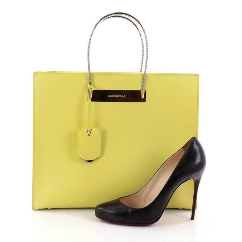 This authentic Balenciaga Cable Shopper Tote Leather Medium is a bag that's simple in shape but bold in color. Crafted from neon yellow leather, this structured bag features silver cable tote handles, logo-embossed golden plate and gold and