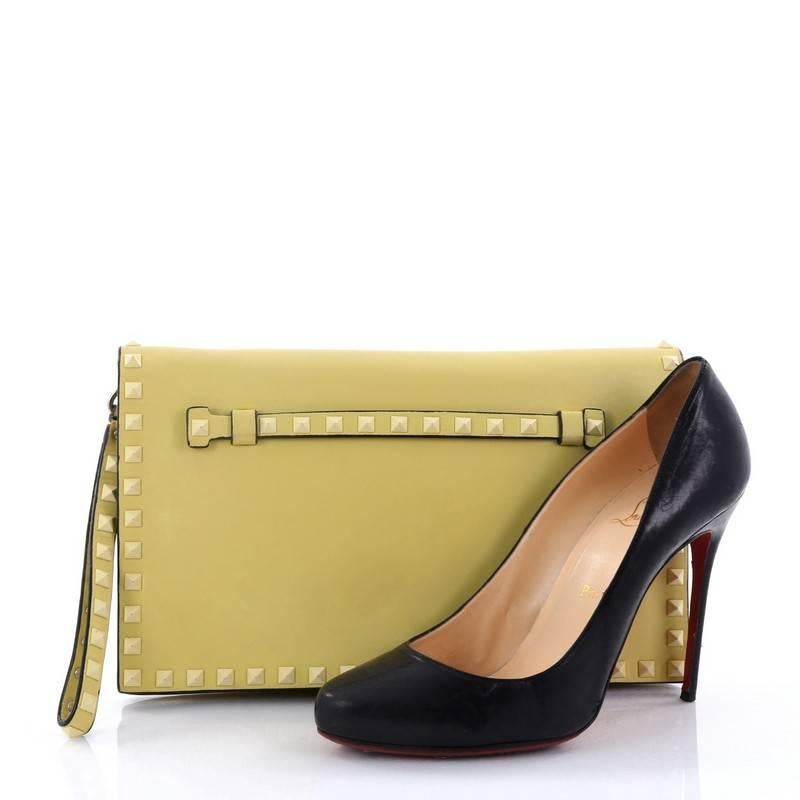 This authentic Valentino Rockstud Flap Clutch Leather is a chic yet functional accessory perfect for on-the-go moments. Crafted from yellow leather, this trendy clutch features a leather hand sling, studded hand strap, polished gold Valentino