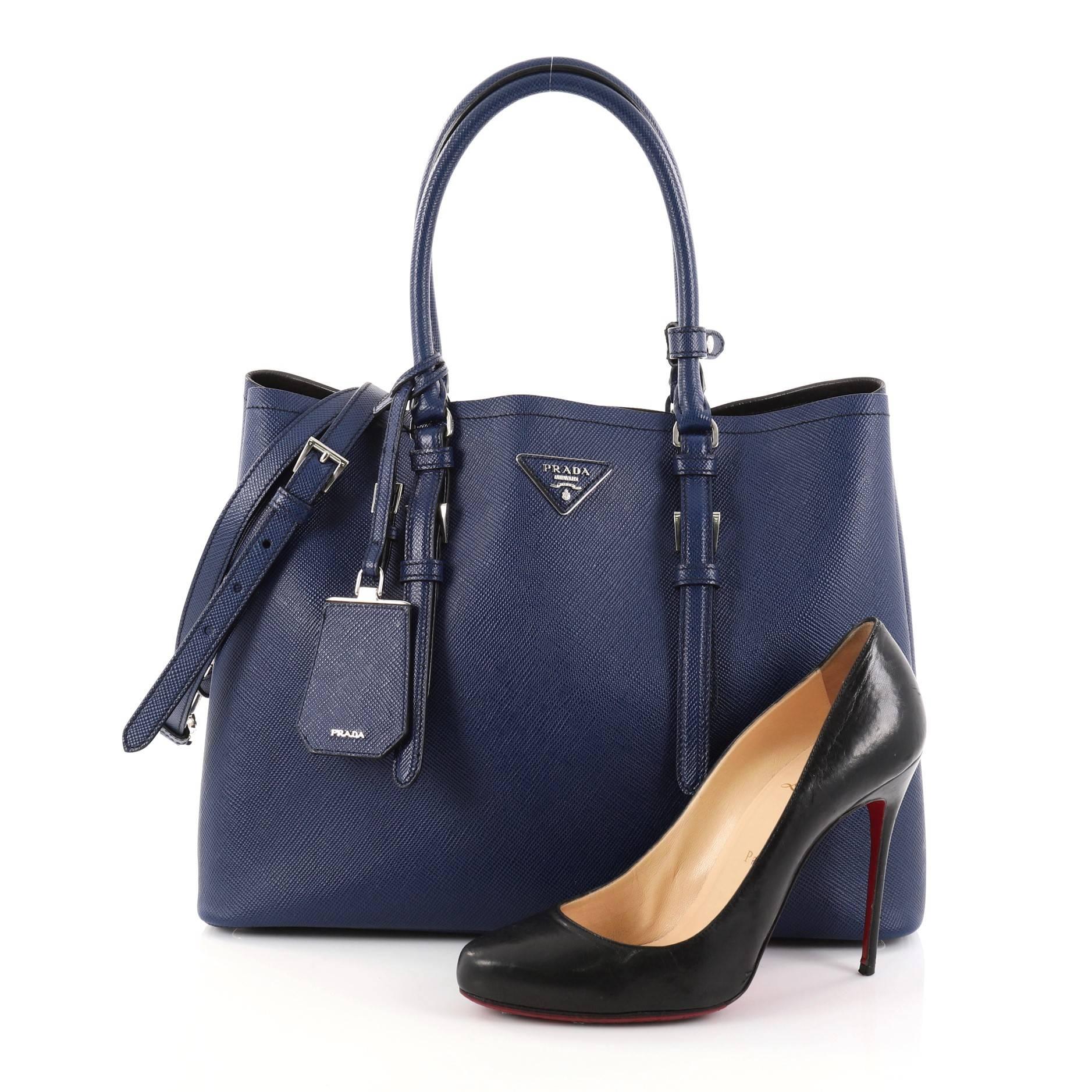 This authentic Prada Cuir Double Tote Saffiano Leather Medium is elegant in its simplicity and structure. Crafted from sturdy dark blue saffiano leather, this tote features dual-rolled handles, side snap buttons, Prada's trademark triangle logo at