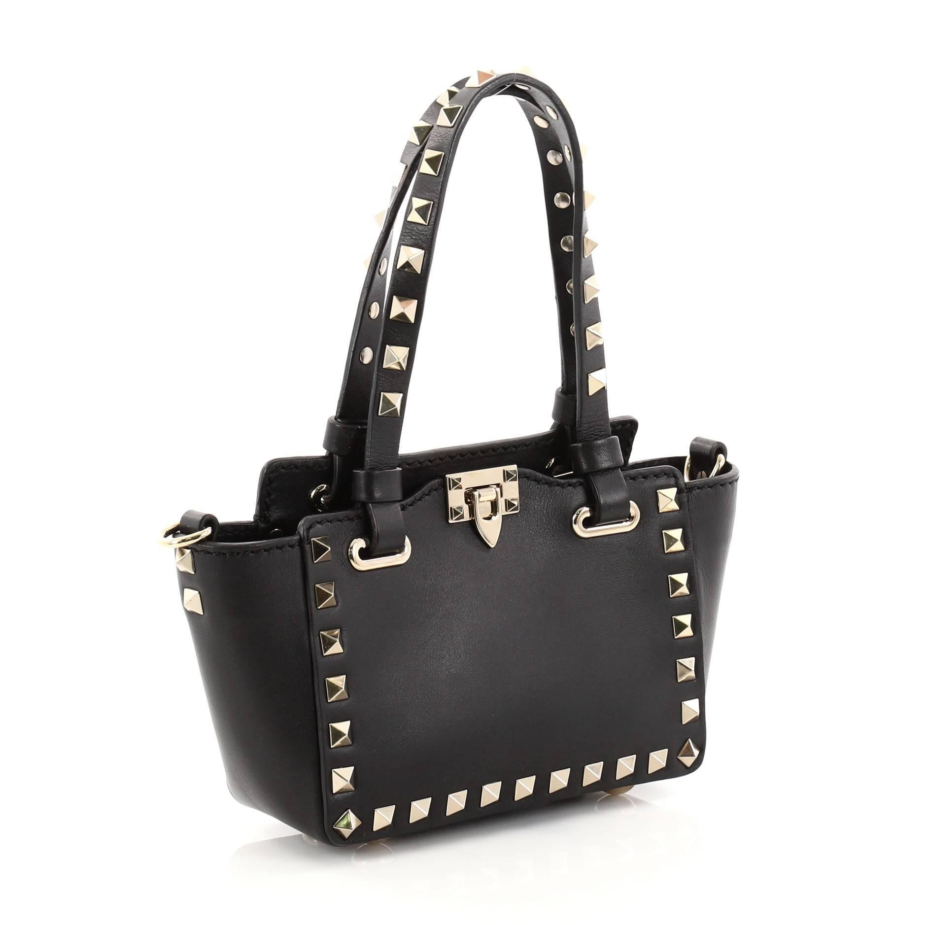This authentic Valentino Rockstud Tote Soft Leather Micro mixes edgy style with luxurious detailing. Crafted from black soft leather, this stylish tote features dual tall flat handles, gold-tone pyramid stud trim details, a signature clasp