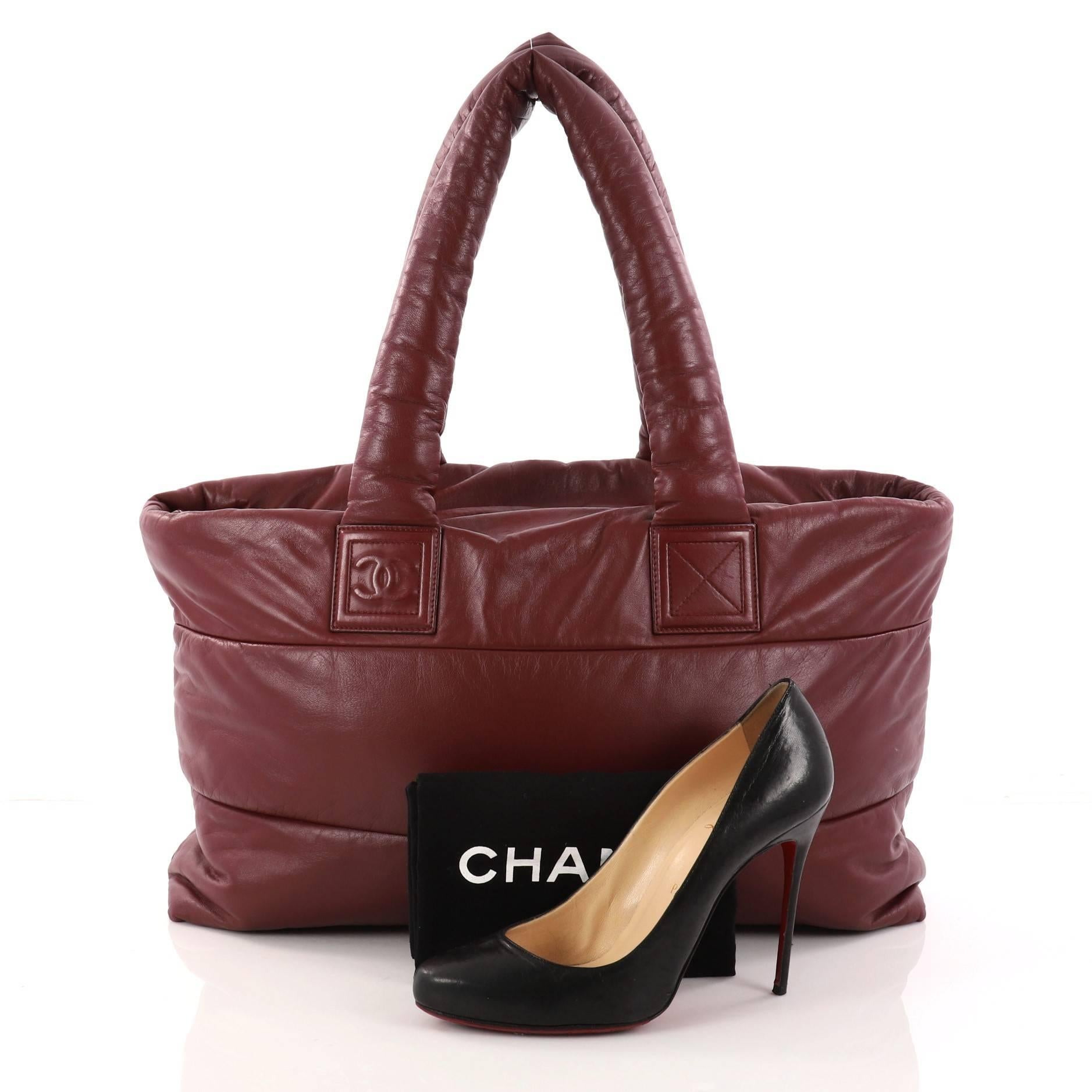This authentic Chanel Coco Cocoon Zipped Tote Lambskin Large is a highly sought-after piece from Lagerfeld's fun and chic Coco Cocoon line. Crafted from dark red lambskin leather, this sporty tote features padded top handles, interlocking CC logo
