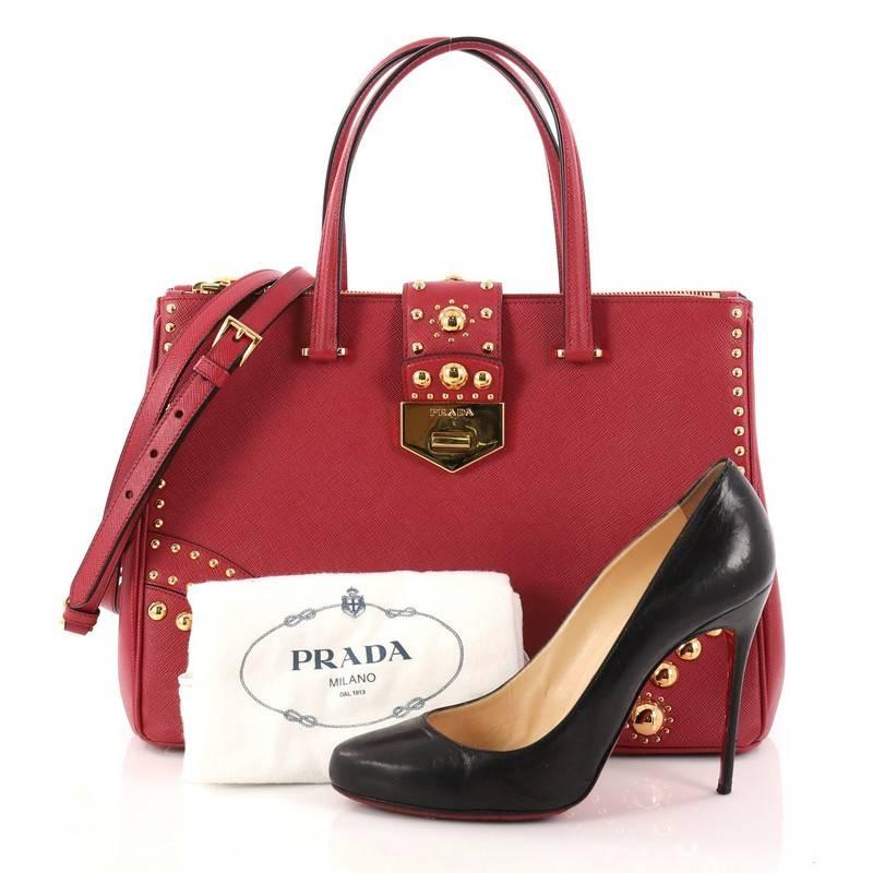 This authentic Prada Turnlock Double Zip Tote Studded Saffiano Leather Medium is a stylish bag perfect to carry around from day to night. Crafted in red saffiano leather, this tote features multiple gold studs, dual leather handles, detachable