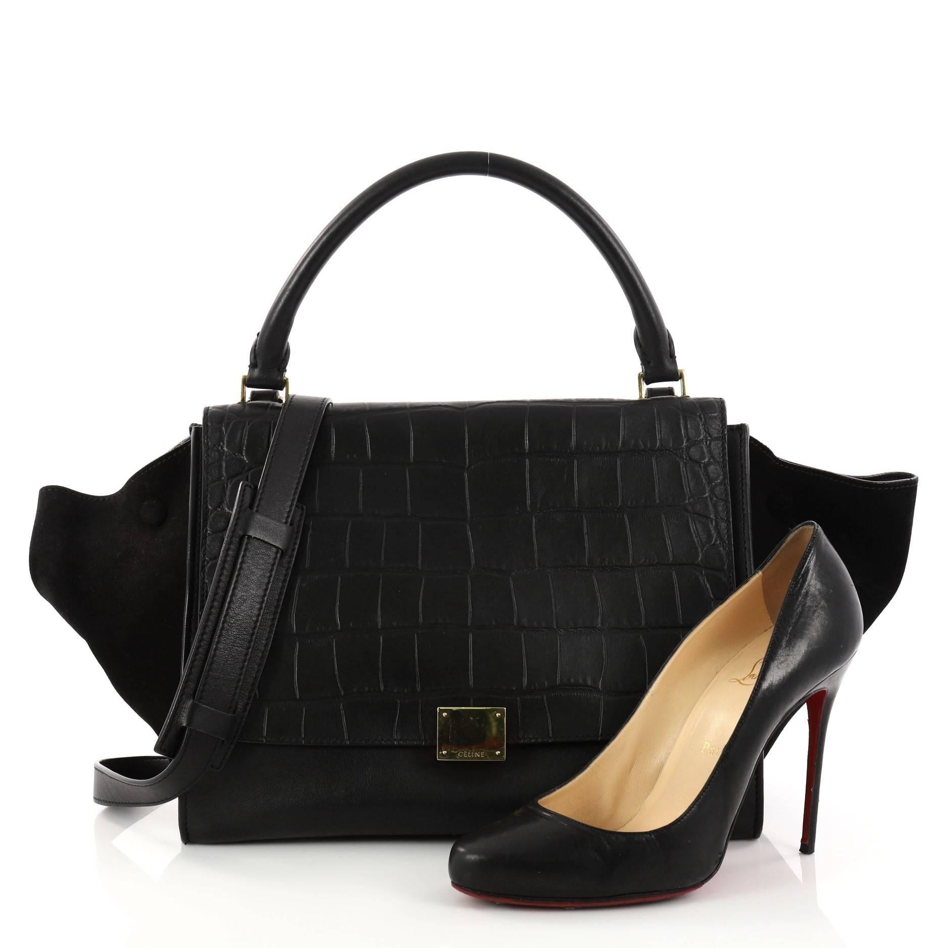 This authentic Celine Trapeze Handbag Crocodile Embossed Leather Medium is a fashionista's dream bag. Crafted from black crocodile embossed leather with black suede wings, this bag features top rolled leather handle, side wings snap closures,