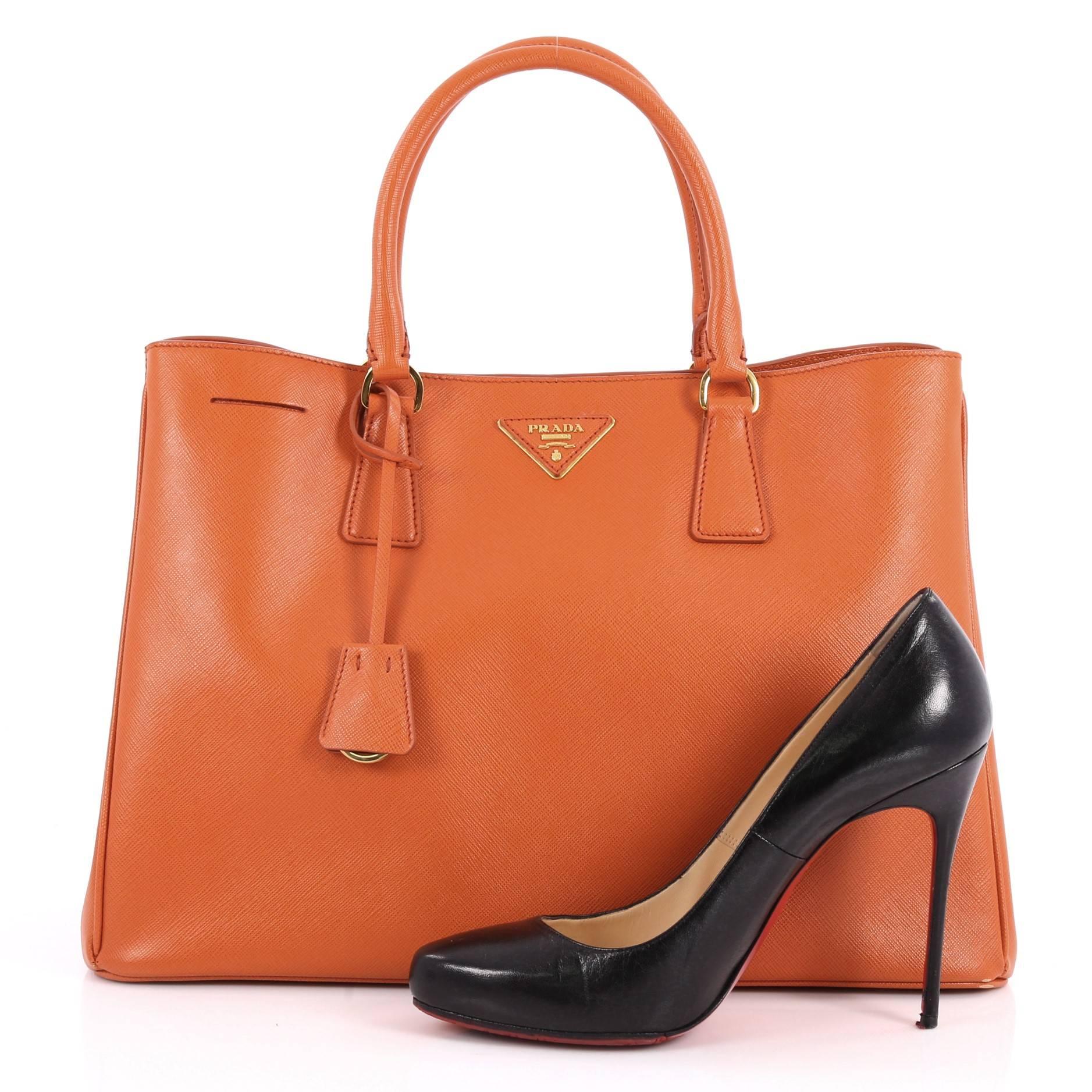 This authentic Prada Lux Open Tote Saffiano Leather Medium is elegant in its simplicity and structure. Crafted from orange saffiano leather, this sturdy and spacious tote features dual-rolled handles, gusseted side with snap buttons, iconic Prada