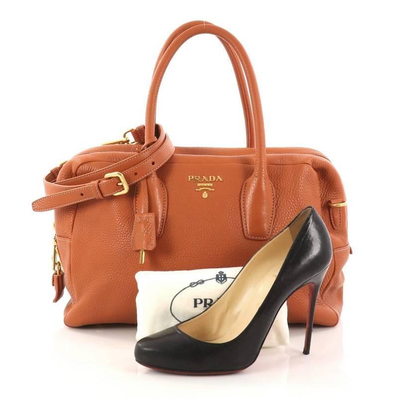 This authentic Prada Convertible Bauletto Bag Vitello Daino Medium exudes a stylish and industrial design made for everyday excursions. Crafted from orange vitello daino leather, this exquisite bag features dual-rolled handles, raised Prada Milano