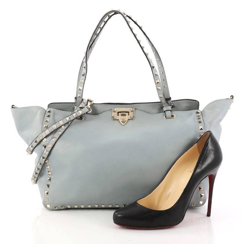 This authentic Valentino Rockstud Tote Soft Leather Medium mixes edgy style with luxurious detailing. Crafted from light blue soft leather, this stylish tote features dual tall flat handles, gold-tone pyramid stud trim details, signature clasp lock,