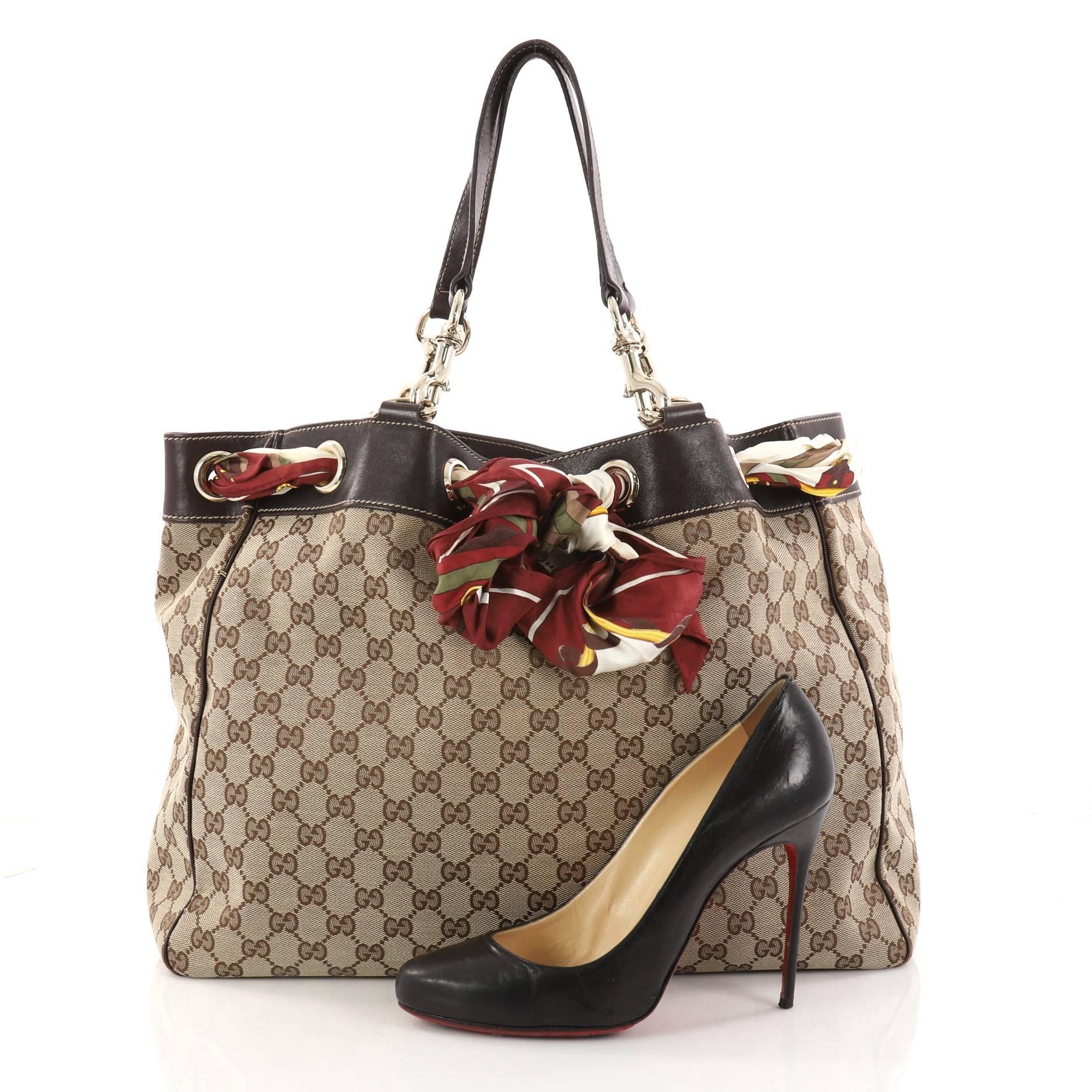 This authentic Gucci Positano Tote GG Canvas Large is a striking tote for on-the-go moments. Crafted from brown GG canvas, this chic tote features dark brown leather trims, iconic printed Gucci silk scarf threaded through grommets, dual flat leather